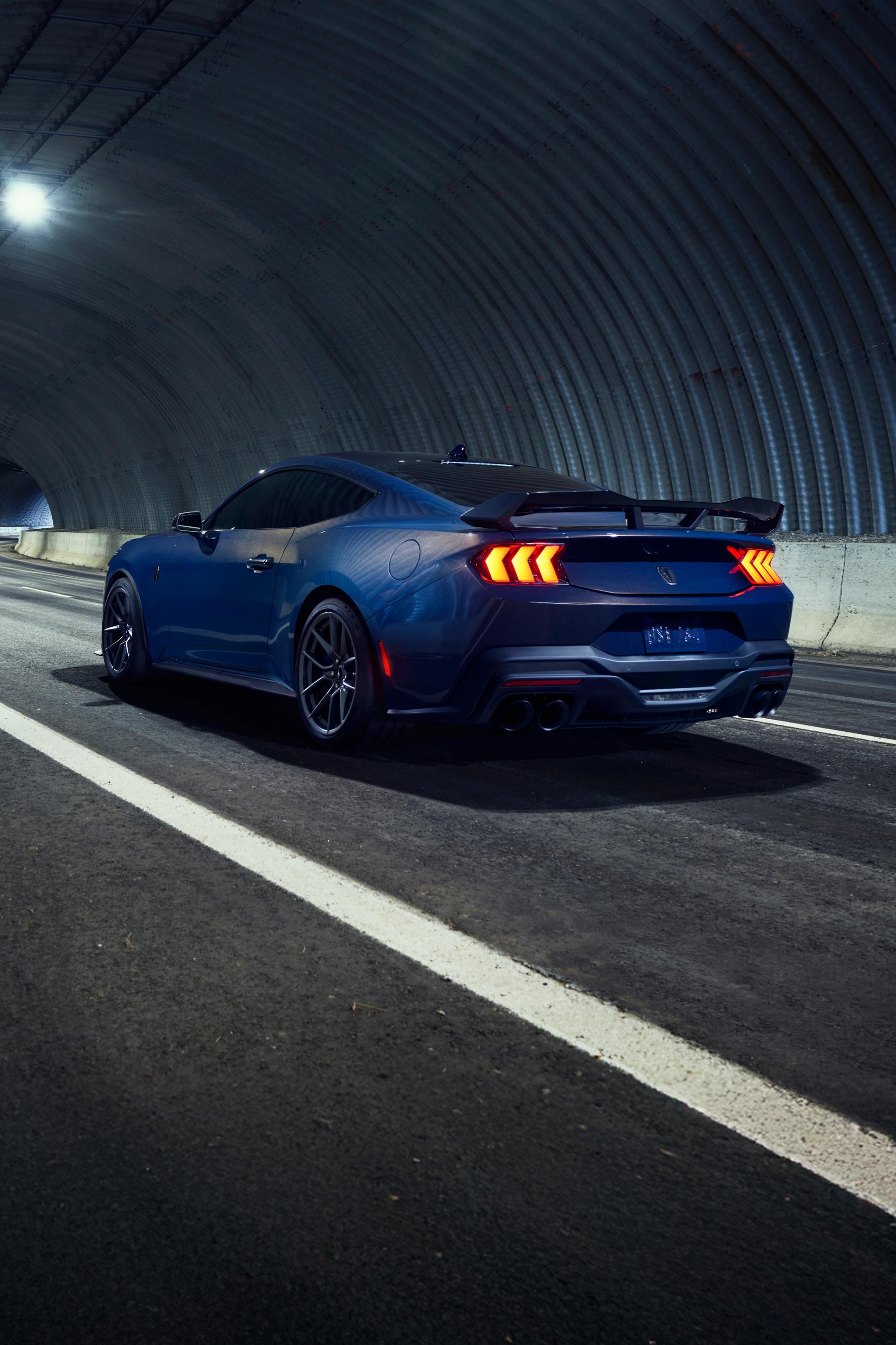 A blue 2025 Ford Mustang being driven down a paved tunnel at night